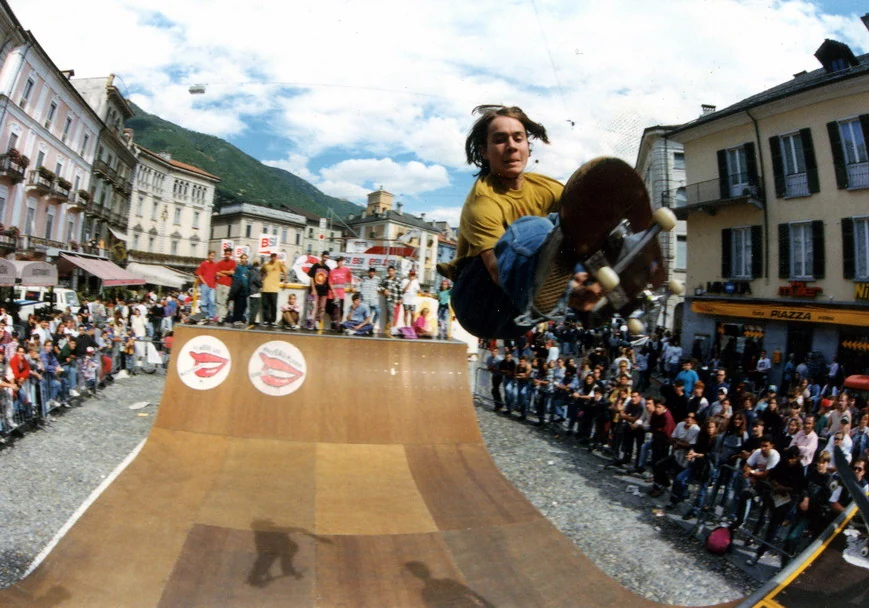 Skateboarder beim Frontside Stalefish über einer Minirampe auf der Piazza Grande in Locarno, umgeben von dichtem Publikum.
