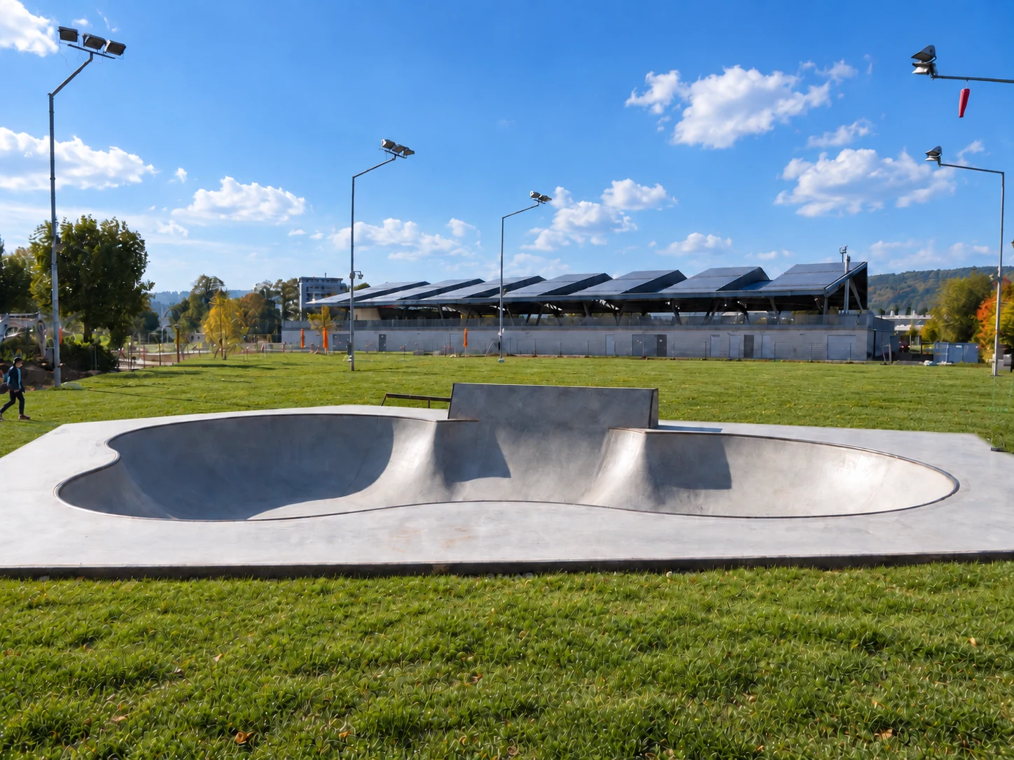 Beton-Bowl im Sportpark Bünzmatt in Wohlen, umgeben von Rasenflächen, mit einer Halle und Flutlichtmasten im Hintergrund.