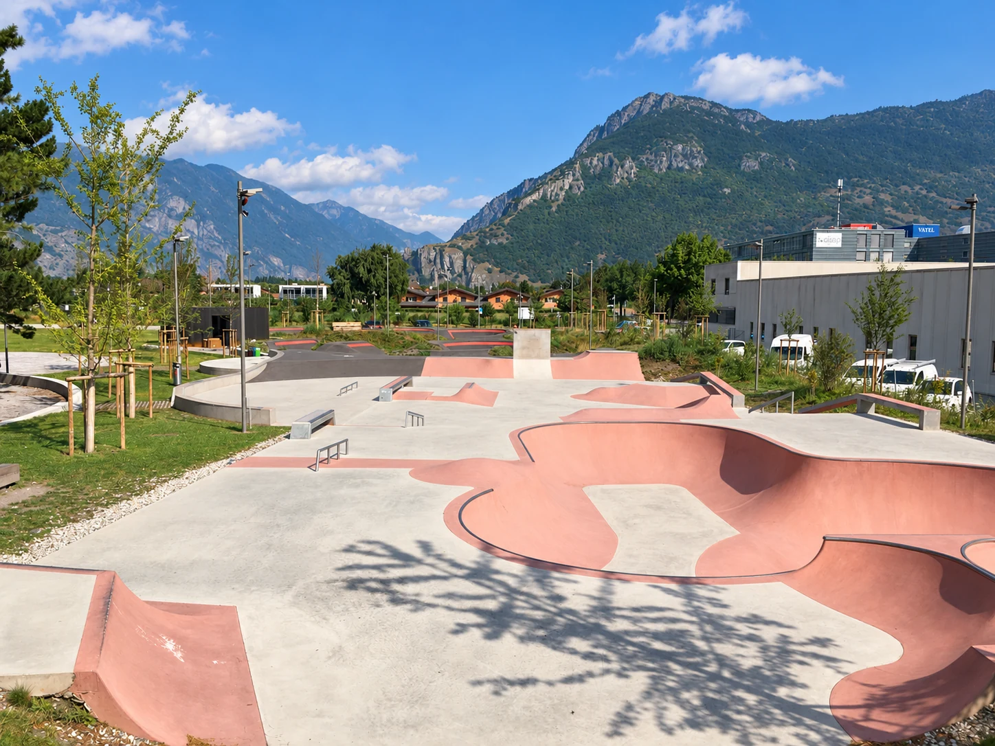Leerer Beton-Skatepark mit grosser rosafarbener Bowl und Street-Bereich vor sonnigem Alpenpanorama.