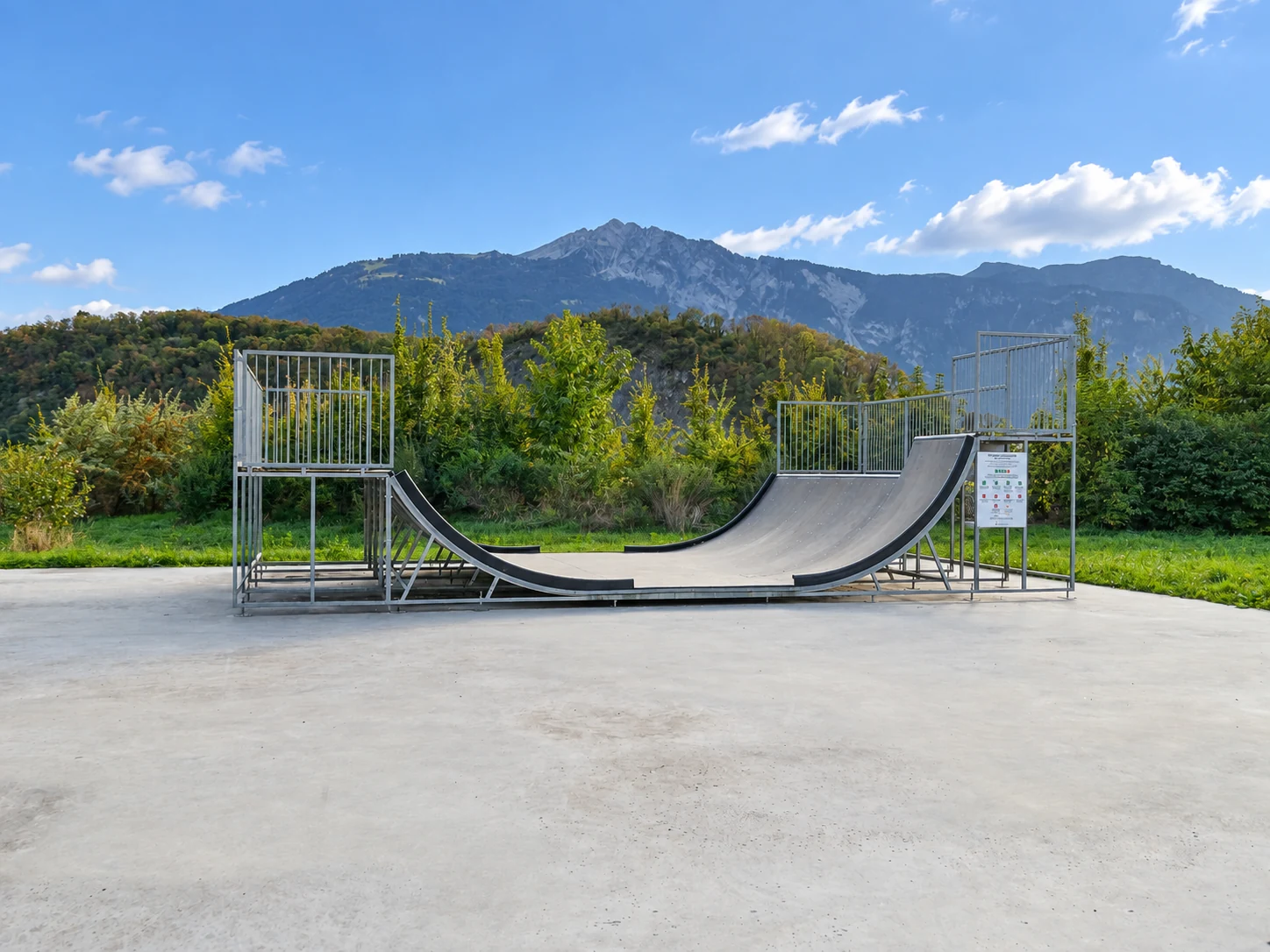 Minirampe Ollon – Seitenansicht mit Extension Seitliche Gesamtansicht der Minirampe in Ollon mit erhöhtem Rampenabschnitt, Hinweisschild und Berglandschaft im Hintergrund.