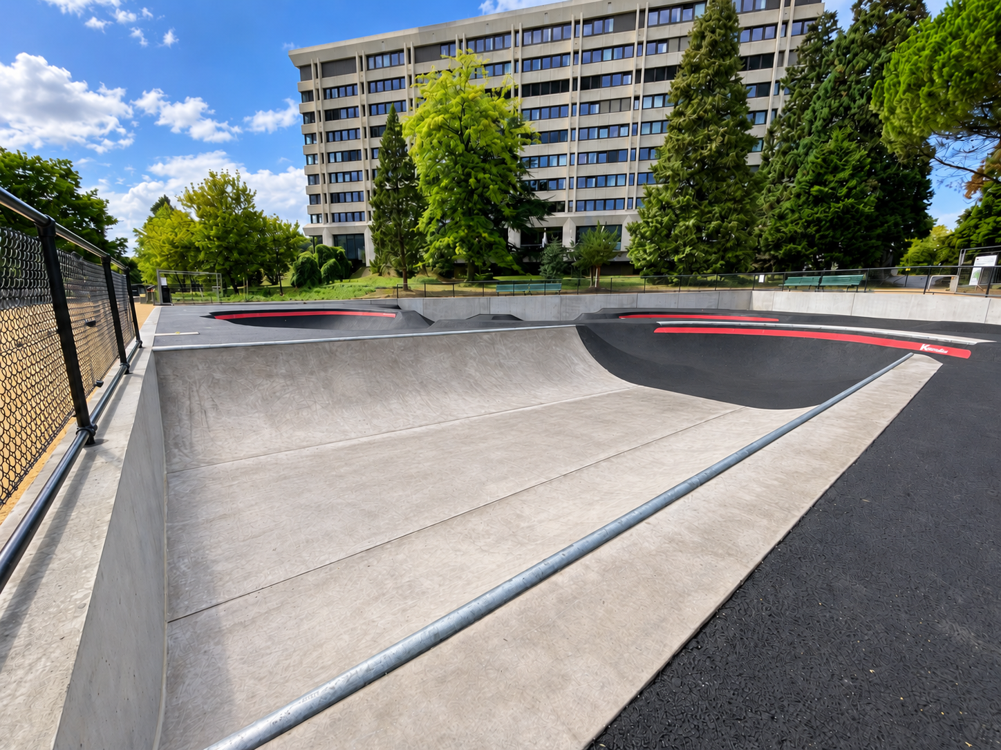 Seitlicher Blick auf die Beton-Miniramp im Parc des Franchises in Genf mit diagonal verlaufendem Metallcoping und angrenzendem Pumptrack.