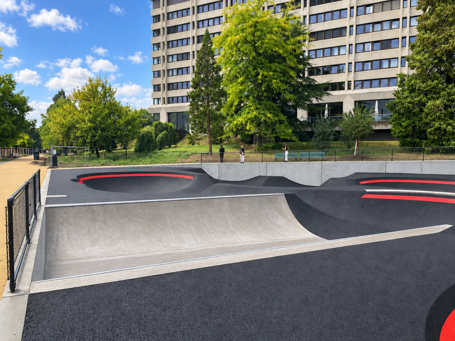 Beton-Miniramp und Asphalt-Pumptrack im Parc des Franchises in Genf mit roten Kurvenmarkierungen und drei Personen am hinteren Geländer.